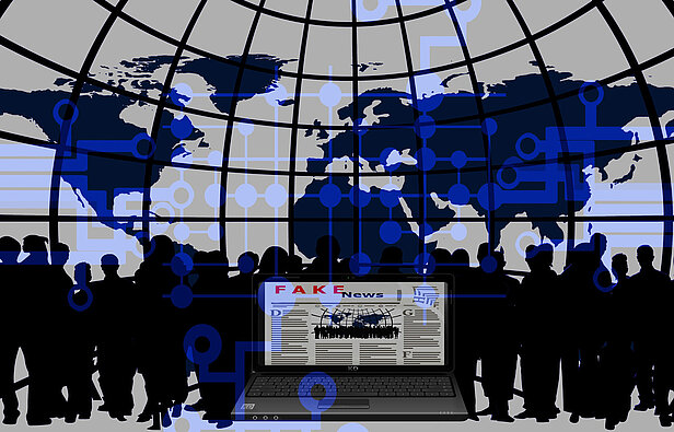 Ein Laptop, auf dem eine Nachrichtenseite mit der Überschrift „FAKE News“ in Rot angezeigt wird, ist von Silhouetten von Menschen umgeben. Im Hintergrund ist eine Weltkarte von einem Netzgitter umschlossen, überlagert von blauen Netzwerkverbindungen und digitalen Symbolen.
